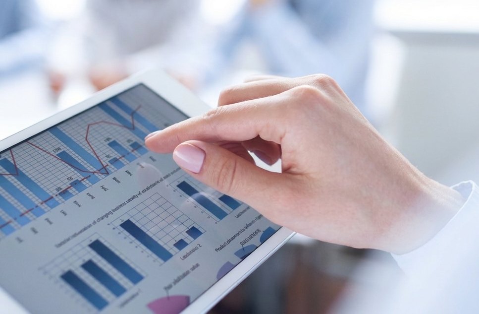Hand pointing at financial charts on a tablet during a team meeting